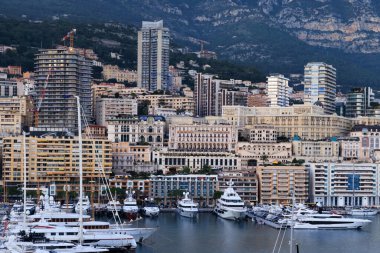 Monako 'nun lüks limanının yakın plan görüntüsü, görkemli binalar, gösterişli yatlar, ve modern mimari arkaplan ormanlık dağlara ve canlı şehir yaşamına karşı.