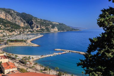Menton 'un göz kamaştırıcı panoramik manzarası. Gök mavisi Akdeniz, kumlu plajlar, canlı bir marina ve açık mavi gökyüzünün altındaki yemyeşil tepeler. Cote d Azur, Fransa