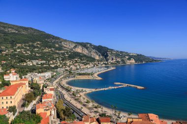 Menton 'un göz kamaştırıcı panoramik manzarası. Gök mavisi Akdeniz, kumlu plajlar, canlı bir marina ve açık mavi gökyüzünün altındaki yemyeşil tepeler. Cote d Azur, Fransa