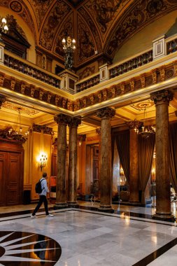 Monte Carlo, Monaco - 01 Kasım 2024: Monako 'daki Monte Carlo kumarhanesinin içinde mermer sütunlar, altın sütunlar, avizeler ve karmaşık tavan sanatının yer aldığı büyük bir salon. Bir ziyaretçi lüks iç mekanda yürüyor..
