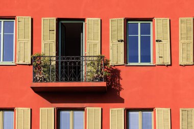 Nice, Fransa 'da canlı kırmızı ve sarı bir bina, klasik yeşil kepenkler, dekoratif pencere çerçeveleri ve zarif siyah işlemeli demir balkon içerir.. 