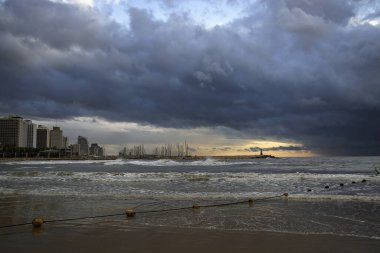 Tel Aviv 'de kış denizi. Kara bulutlar gökyüzünü kaplıyor, dalgalar yavaşça kıyıya dokunuyor, ve sarı şamandıralı bir ip suya uzanıyor..