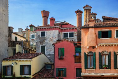 Süslü bacaları, kırsal dokuları ve açık mavi gökyüzünün altında tünemiş bir martı olan geleneksel Venedik çatıları..