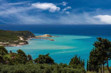 Yunanistan 'ın Korfu Adası' nın turkuaz kıyı şeridinin güzel panoramik manzarası, yemyeşil ve çarpıcı mavi deniz altında canlı bir gökyüzü altında.