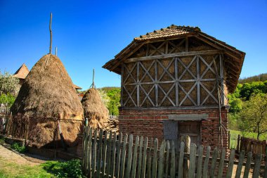 Geleneksel saman ambarı ve bir Romanya köyünde koni şeklinde saman yığınları. Kırsal kırsal mimari, mavi gökyüzü ve Doğu Avrupa 'da bahar yeşilliği.