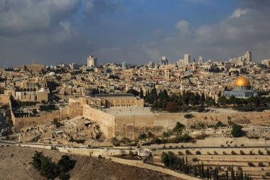Kudüs 'ün panoramik manzarası ikonik altın kubbe, antik taş binalar ve parçalı bulutlu gökyüzünün altında dramatik bir siluet..