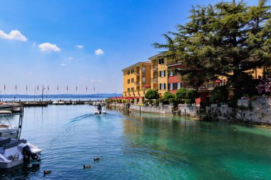 Renkli binalar, tekneler, berrak turkuaz su ve İtalya 'nın Garda Gölü' nde huzurlu bir yaz atmosferi olan Sirmione rıhtımı manzarası..