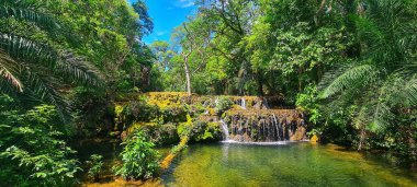 hidden waterfall on a sunny day in the woods with blue sky clipart