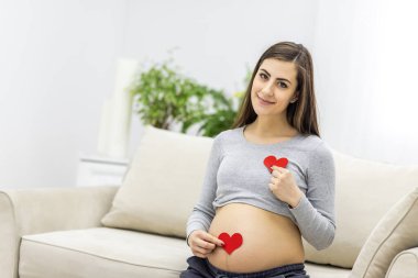 Kırmızı kalbi elinde tutan hamile bir kadının fotoğrafı. Hamile kadın kavramı.