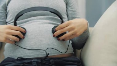 Karnında kulaklık olan hamile bir kadının 4K yavaş çekim videosu. Hamile kadın düşüncesi.