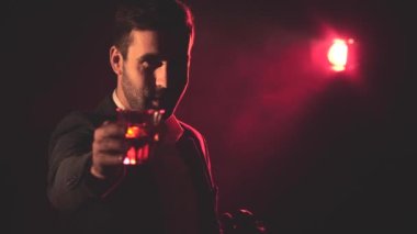 4K yavaş çekim videosunda takım elbiseli sigara içen adam ve arka planda pembe ışık. Sigara içen adam kavramı.