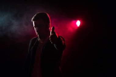 Gülümseyen bir adamın pembe ışıkla baş parmağının göründüğü fotoğraf. Başparmağı havada insan kavramı.