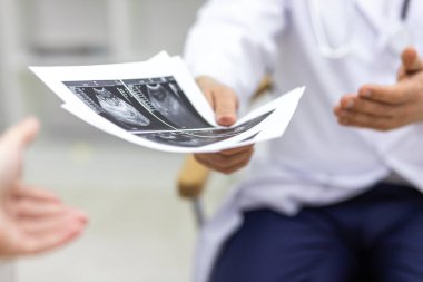 Doktorun laboratuvar önlüğü giyerken çekilmiş fotoğrafı hastasına ultrason sonuçlarını gösteriyor. Sağlık hizmetleri kavramı.