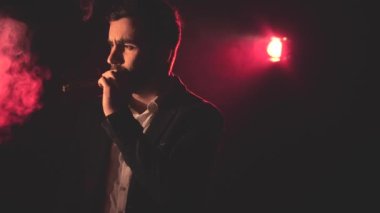 4K yavaş çekim videosunda takım elbiseli sigara içen adam ve arka planda pembe ışık. Sigara içen adam kavramı.