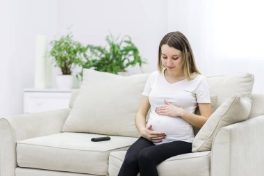 Pregnant woman looking at her belly on white sofa. Concept of pregnant woman.