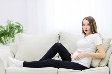 Facial expression of pregnant woman on white sofa. Concept of pregnant woman.