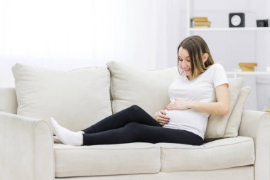 Pregnant woman put her hands on her stomach on white sofa. Concept of pregnant woman.