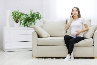 Photo of cute pregnant woman sitting on sofa. Concept of pregnant woman.