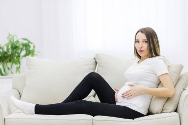 Facial expression of pregnant woman on white sofa. Concept of pregnant woman.