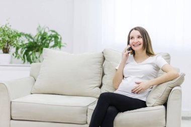 Pregnant woman talking over the phone on white sofa. Concept of pregnant woman.