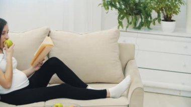 4k slowmotion video of pregnant woman eating an apple and reading a book. Concept of pregnant woman.