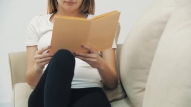 Hamile bir kadının kitap okuyup karnına dokunduğu 4K yavaş çekim videosu. Hamile kadın kavramı.
