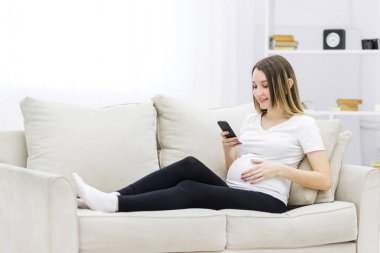 Young pregnant woman on white sofa using phone. Concept of pregnant woman.