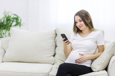 Pregnant woman wearing white t-shirt looking at the phone. Concept of pregnant woman.