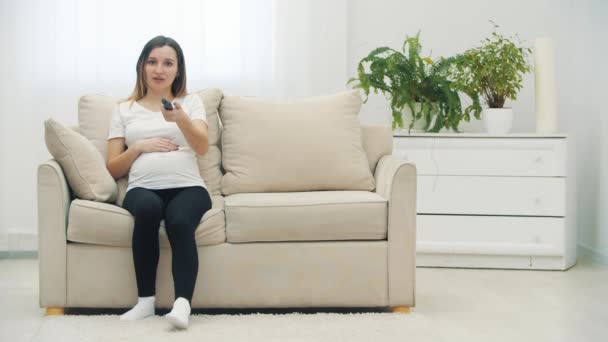 Видео Беременной Женщины Сидящей Белом Диване Дистанционным Управлением Концепция Беременной — стоковое видео