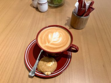 Ahşap masada kahve ve kapuçino. Bir fincan kapuçinonun yakın plan fotoğrafı. Üstünde ocak şeklinde süt var. Kafe titreşimleri kavramı