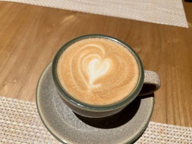 Tahta arka planda kalbi olan bir fincan kahve. Kurabiye ve metal kaşıkla ahşap masada izole edilmiş bir fincan kahve.