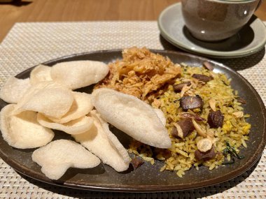 Tabakta kızarmış pilav, bir fincan kahve ve ahşap masada kraker..