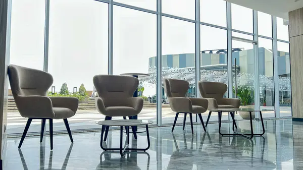 Modern lobi iç mekanı, ahşap duvar ve mermer döşemeler tasarımcı koltuğu ve panoramik cam pencereli küçük masa.