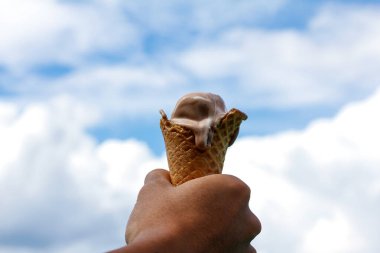 Adamın eli dondurma tutarken, arkasında bulutlar vardı.