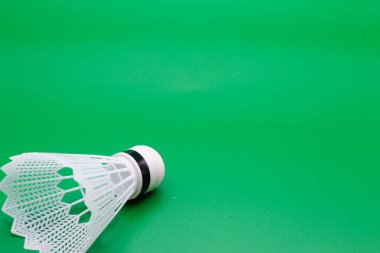 Beyaz tüyler ve kırmızı yakalı tek bir badminton mekik çükünün yüksek kaliteli görüntüsü, geniş bir kopya alanı olan saf yeşil arka planda belirgin bir şekilde sergilenmektedir.