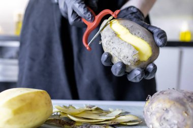 Patates soymak. Taze çiğ patates ve soyucu masada, yakın plan.