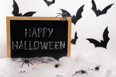 A chalkboard with the inscription Happy Halloween on a background of bats. Spiders in a web in the foreground  clipart