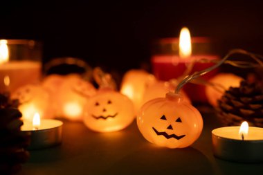 Fener şeklinde bir balkabağı. Bayram havası. Arka planda mumlar ve koniler var. Balkabağına yakın çekim