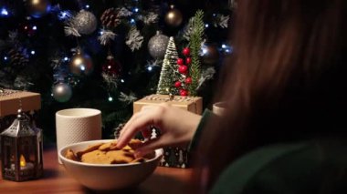 Masadaki ağacın yanında Noel kurabiyesi yiyen bir kız. Yeni Yıl ve Noel