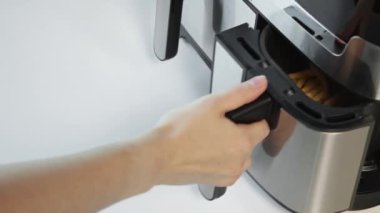 Kadın kızartma sepetini açar ve onları maşayla karıştırır.