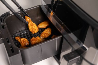 Chicken wings in air fryer being lifted with tongs, golden and crispy after cooking clipart