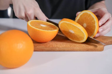 Tahtadaki bıçakla taze portakal dilimleri kesmek, sağlıklı atıştırmalık hazırlamak.