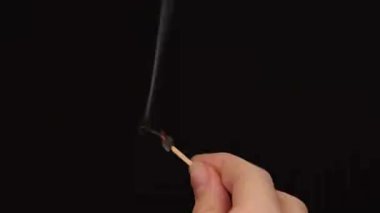 Elinde yanan bir kibrit çöpü, siyah bir arka planda dumanla yukarı doğru gidiyor.
