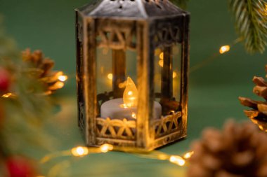 antique lantern with a glowing candle surrounded by pinecones and fairy lights, festive and warm holiday atmosphere clipart