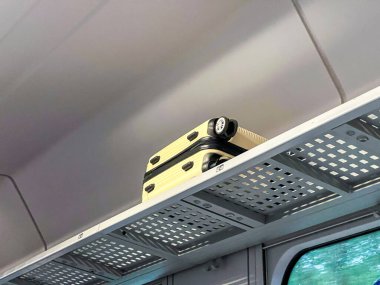 Sarı bavul bir tren kompartımanındaki bagaj rafına yerleştirilmiş. Seyahat sahnesi, minimalist iç mekan. 