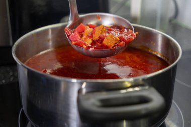 Mutfak ocağındaki büyük bir tencereden sebzeli çorba kepçesi.