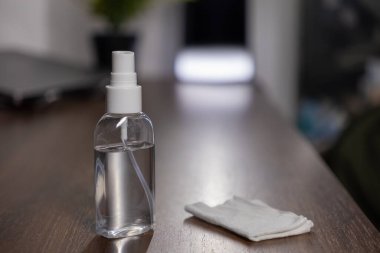 Şeffaf sprey şişesi ve katlanmış beyaz bez. Temizlik ve dezenfeksiyon için cilalanmış ahşap bir yüzey.