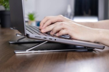 Eller dizüstü bilgisayarda, ergonomik duruşu olan, temiz ve düzenli bir çalışma alanındaki ahşap bir masada, geliştirilmiş duruş için yazı yazıyor.