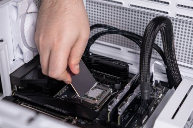 spreading thermal paste evenly on cpu surface during pc assembly, hand using a tool for precise application, close-up on motherboard and processor clipart