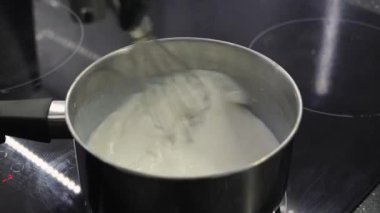 Fırının üstünde paslanmaz çelik bir tencerede beyaz bir sos çırpmak, pürüzsüz ve kaymak gibi kıvamında pişirmek.
